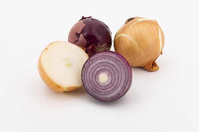 A selection of different colored onions, some cut to reveal the layers inside
